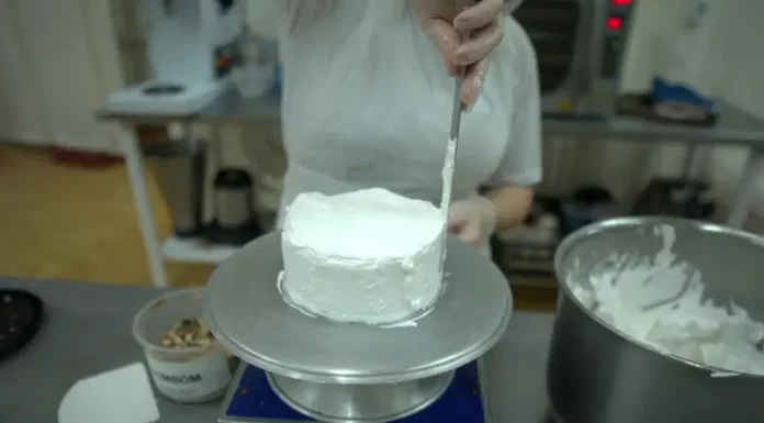 Pessoa realiza trabalho de confeitaria ao aplicar cobertura em um bolo na cozinha de uma unidade prisional, durante atividade de capacitação profissional.