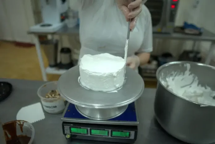 detentas trabalhando Pessoa realiza trabalho de confeitaria ao aplicar cobertura em um bolo na cozinha de uma unidade prisional, durante atividade de capacitação profissional.