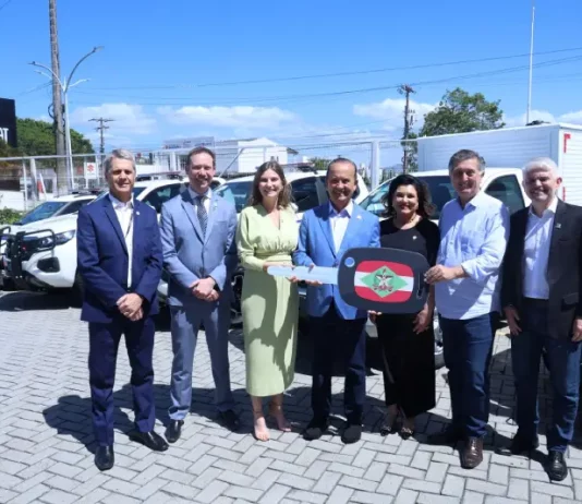 Governador lança Programa Identidade Catarina e entrega novas viaturas à Polícia Científica Foto mostra o governador de Santa Catarina, ao lado de autoridades, entregando a chave simbólica das novas viaturas à Polícia Científica durante o lançamento do Programa Identidade Catarina, simbolizando o investimento na modernização da segurança pública.