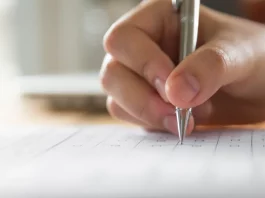 Mão de estudante preenchendo o cartão resposta do Enem, simbolizando a preparação para a prova.