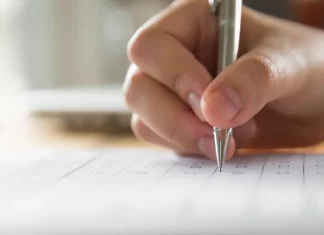 Mão de estudante preenchendo o cartão resposta do Enem, simbolizando a preparação para a prova.