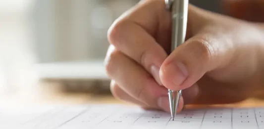 Faculdade Anhanguera de São José realiza aulão preparatório gratuito para o Enem Mão de estudante preenchendo o cartão resposta do Enem, simbolizando a preparação para a prova.