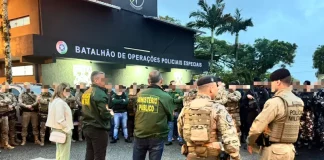 A imagem mostra o efetivo reunido em frente ao Batalhão de Operações Policiais Especiais antes do início da Operação Free Way. A cena registra o alinhamento das equipes do GAECO, Ministério Público e Polícia Militar, evidenciando a preparação conjunta para o cumprimento dos mandados e para a atuação coordenada no combate ao tráfico de drogas na Grande Florianópolis.