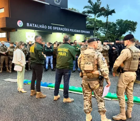A imagem mostra o efetivo reunido em frente ao Batalhão de Operações Policiais Especiais antes do início da Operação Free Way. A cena registra o alinhamento das equipes do GAECO, Ministério Público e Polícia Militar, evidenciando a preparação conjunta para o cumprimento dos mandados e para a atuação coordenada no combate ao tráfico de drogas na Grande Florianópolis.