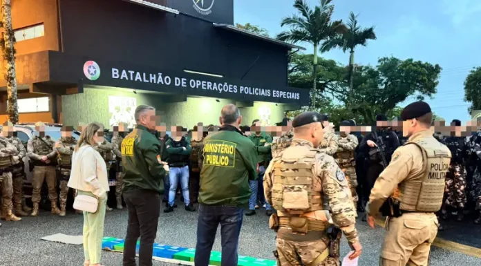 A imagem mostra o efetivo reunido em frente ao Batalhão de Operações Policiais Especiais antes do início da Operação Free Way. A cena registra o alinhamento das equipes do GAECO, Ministério Público e Polícia Militar, evidenciando a preparação conjunta para o cumprimento dos mandados e para a atuação coordenada no combate ao tráfico de drogas na Grande Florianópolis.
