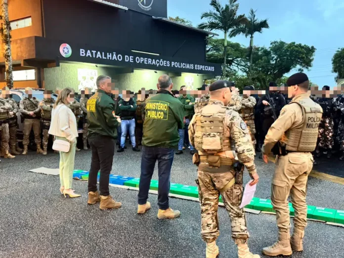 A imagem mostra o efetivo reunido em frente ao Batalhão de Operações Policiais Especiais antes do início da Operação Free Way. A cena registra o alinhamento das equipes do GAECO, Ministério Público e Polícia Militar, evidenciando a preparação conjunta para o cumprimento dos mandados e para a atuação coordenada no combate ao tráfico de drogas na Grande Florianópolis.