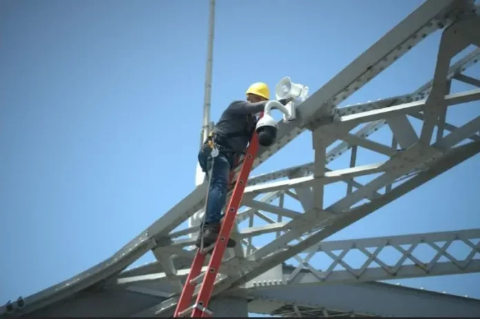 Trabalhador instala uma câmera de monitoramento na estrutura da Ponte Hercílio Luz para reforçar a segurança com tecnologia de vigilância.
