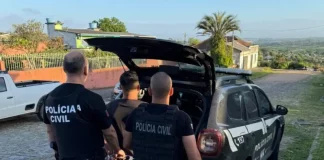 Policiais conduzem um homem preso até a viatura durante operação de combate a fraudes em sistemas digitais.