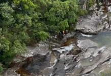 Bombeiros resgatam adolescente após queda na Cachoeira do Jarrão, em Palhoça Imagem mostra bombeiros realizando o resgate de uma adolescente ferida em área de cachoeira, ilustrando a operação em terreno íngreme e de difícil acesso.