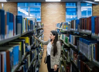 Aluna do Universidade Gratuita em uma biblioteca escolhendo livros, ilustrando o acesso ampliado à educação.