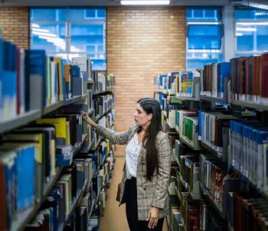 Aluna do Universidade Gratuita em uma biblioteca escolhendo livros, ilustrando o acesso ampliado à educação.