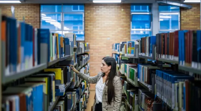Aluna do Universidade Gratuita em uma biblioteca escolhendo livros, ilustrando o acesso ampliado à educação.