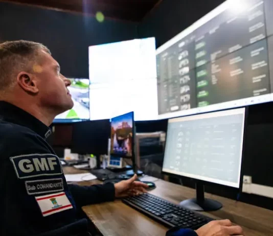 Agente da Guarda Municipal de Florianópolis monitora imagens da cidade em tempo real na central de videomonitoramento, demonstrando o uso de câmeras com tecnologia de reconhecimento facial para reforçar a segurança pública.