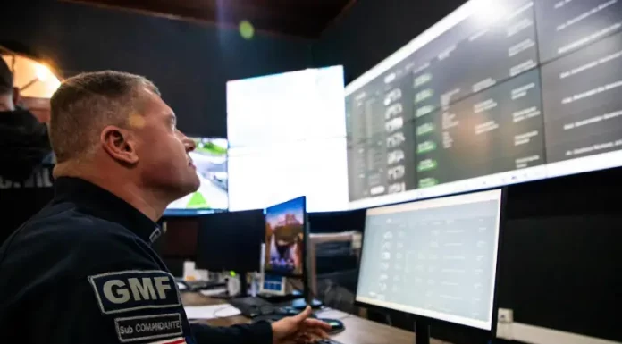 Agente da Guarda Municipal de Florianópolis monitora imagens da cidade em tempo real na central de videomonitoramento, demonstrando o uso de câmeras com tecnologia de reconhecimento facial para reforçar a segurança pública.