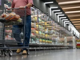 Mulher realizando compras em supermercado, com carrinho contendo alguns produtos, simbolizando o crescimento dos supermercados em 2026