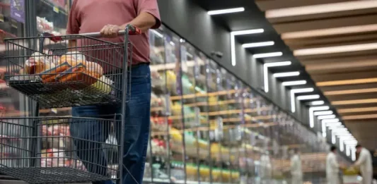 Mulher realizando compras em supermercado, com carrinho contendo alguns produtos, simbolizando o crescimento dos supermercados em 2026