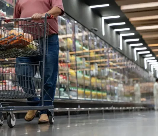 Mulher realizando compras em supermercado, com carrinho contendo alguns produtos, simbolizando o crescimento dos supermercados em 2026