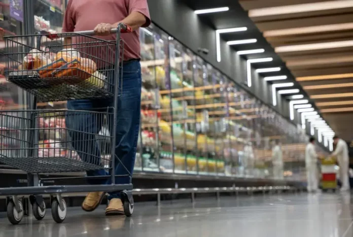 Mulher realizando compras em supermercado, com carrinho contendo alguns produtos, simbolizando o crescimento dos supermercados em 2026