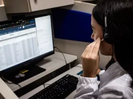 Alô Saúde Floripa oferece atendimento bilíngue 24 horas para turistas Atendente do Alô Saúde Floripa atende ligação de turista enquanto registra informações no computador, mostrando o serviço de suporte médico bilíngue da temporada.