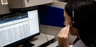 Atendente do Alô Saúde Floripa atende ligação de turista enquanto registra informações no computador, mostrando o serviço de suporte médico bilíngue da temporada.