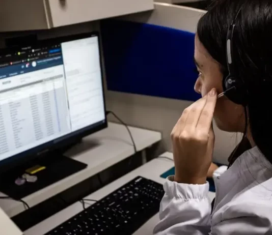 Alô Saúde Floripa oferece atendimento bilíngue 24 horas para turistas Atendente do Alô Saúde Floripa atende ligação de turista enquanto registra informações no computador, mostrando o serviço de suporte médico bilíngue da temporada.