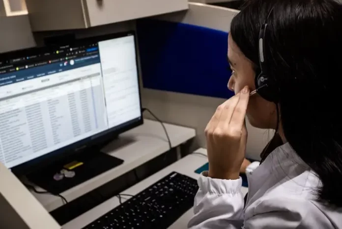 Alô Saúde Floripa Atendente do Alô Saúde Floripa atende ligação de turista enquanto registra informações no computador, mostrando o serviço de suporte médico bilíngue da temporada.