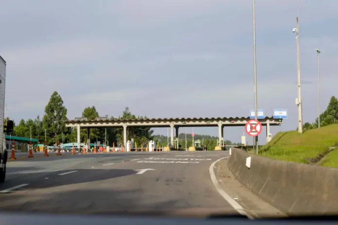 Imagem mostra uma praça de pedágio da Autopista Planalto Sul na BR-116, com cabines de cobrança, sinalização viária e pistas de acesso, ilustrando o local onde os motoristas realizam o pagamento da tarifa.