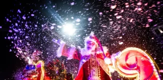 Imagem mostra Papai Noel em um carro alegórico iluminado durante o Desfile de Natal de Florianópolis, com efeitos de neve artificial e luzes, destacando o clima festivo do evento na Beira-Mar Norte.