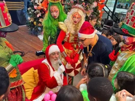 Natal Solidário da Celesc mobiliza voluntários e leva alegria a crianças acolhidas Papai Noel rodeado de crianças durante a ação Natal Solidário da Celesc, ilustrando o momento de confraternização e entrega de presentes.