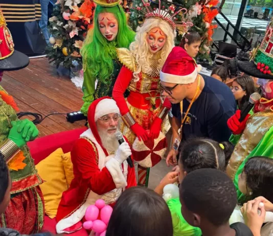 Papai Noel rodeado de crianças durante a ação Natal Solidário da Celesc, ilustrando o momento de confraternização e entrega de presentes.