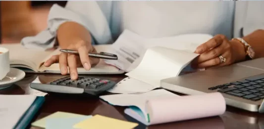 Pessoa confere notas fiscais e faz cálculos com calculadora e notebook, ilustrando a organização necessária para participar da Nota Premiada Josefense.