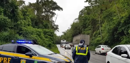 Agente da Polícia Rodoviária Federal ao lado de uma viatura, monitorando o fluxo de veículos nas BRs de Santa Catarina durante o período do Réveillon.