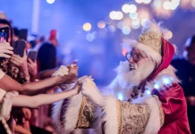 Papai Noel cumprimenta o público durante o Desfile de Natal, interagindo com famílias e celebrando a magia da festa.