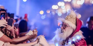 Papai Noel cumprimenta o público durante o Desfile de Natal, interagindo com famílias e celebrando a magia da festa.