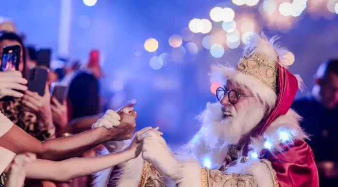Papai Noel cumprimenta o público durante o Desfile de Natal, interagindo com famílias e celebrando a magia da festa.