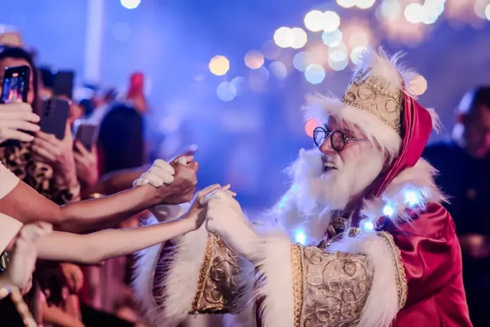 Papai Noel cumprimenta o público durante o Desfile de Natal, interagindo com famílias e celebrando a magia da festa.