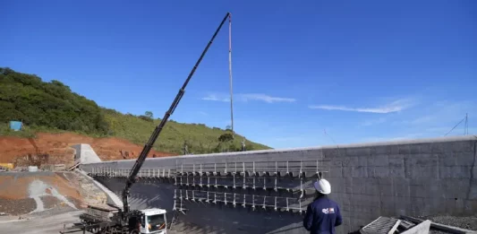 Pessoa com capacete observa obra de usina hidrelétrica em construção, ilustrando o avanço das estruturas ligadas ao Programa Energia Boa.