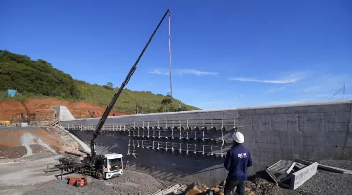 Pessoa com capacete observa obra de usina hidrelétrica em construção, ilustrando o avanço das estruturas ligadas ao Programa Energia Boa.