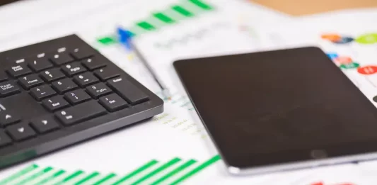 teclado e tablet sobre relatórios financeiros com gráficos, ilustrando análise de dados e planejamento de investimentos públicos