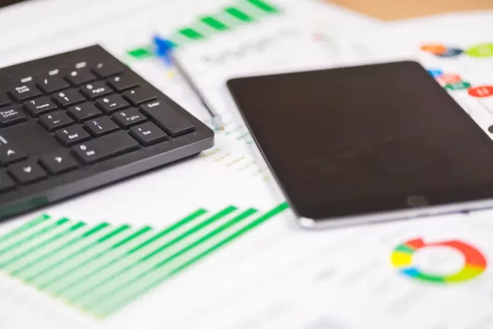 teclado e tablet sobre relatórios financeiros com gráficos, ilustrando análise de dados e planejamento de investimentos públicos