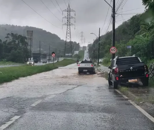 Carros passam por trecho alagado em São José durante a chuva desta terça-feira, ilustrando os impactos do volume intenso de água nas vias do município.