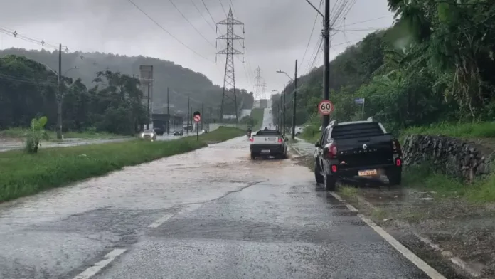 Carros passam por trecho alagado em São José durante a chuva desta terça-feira, ilustrando os impactos do volume intenso de água nas vias do município.