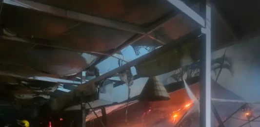 Foto mostra bombeiros atuando no combate ao incêndio dentro do restaurante instalado em uma marina, destacando as chamas ainda ativas e a destruição parcial da estrutura.