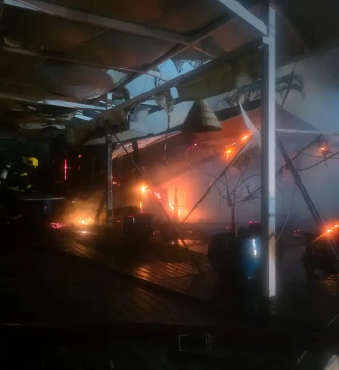 incêndio em marina Foto mostra bombeiros atuando no combate ao incêndio dentro do restaurante instalado em uma marina, destacando as chamas ainda ativas e a destruição parcial da estrutura.