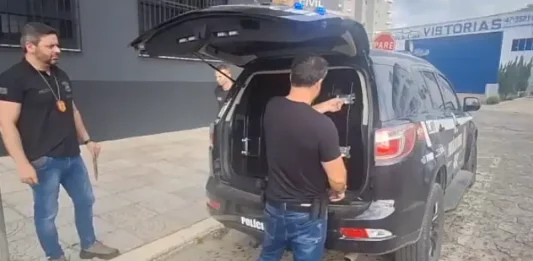 Policiais civis conduzindo homem suspeito de estimular crianças à automutilação.