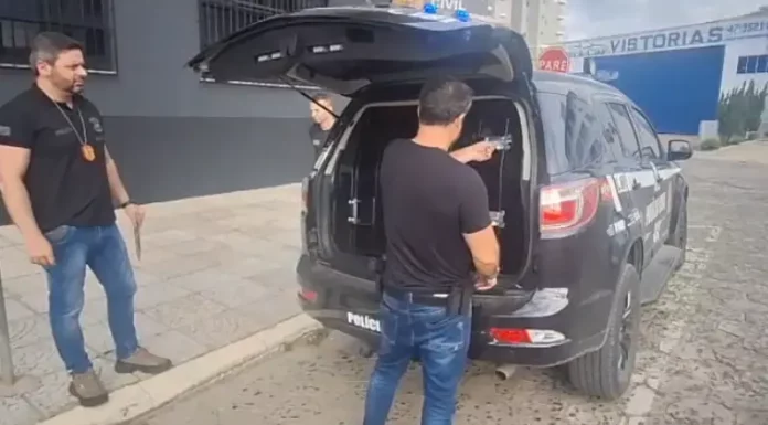 Policiais civis conduzindo homem suspeito de estimular crianças à automutilação.