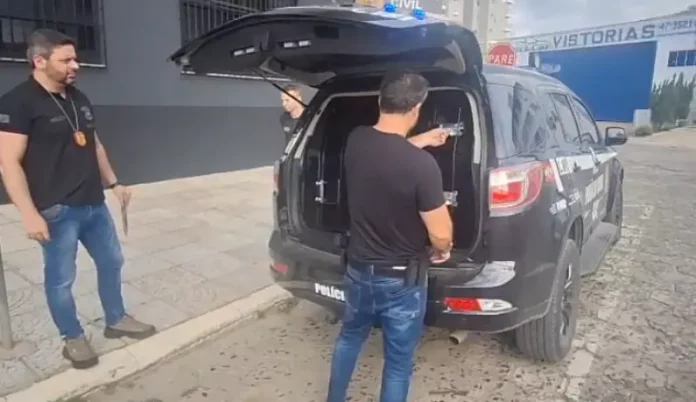 suspeito de estimular crianças à automutilação Policiais civis conduzindo homem suspeito de estimular crianças à automutilação.