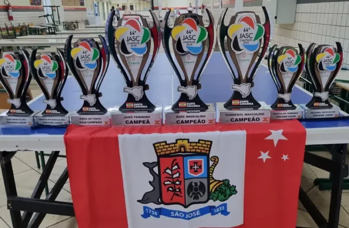 Conjunto de troféus conquistados por São José no Jasc expostos sobre uma mesa, destacando os resultados e o desempenho das equipes do município.