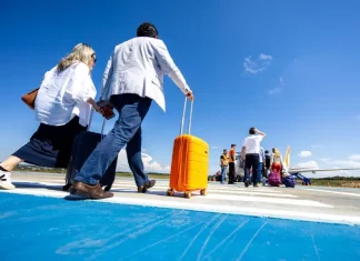 Passageiros caminham pela pista de aeroporto carregando malas e embarcam em aeronave, representando o aumento de passageiros nos aeroportos de Santa Cataina