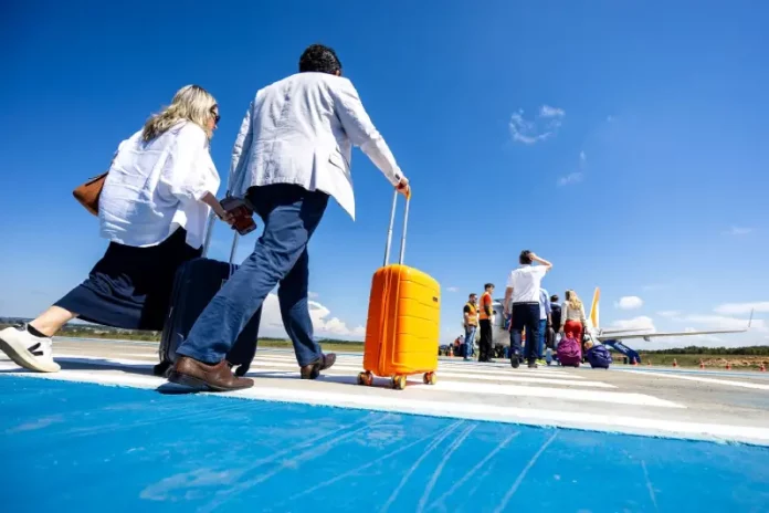 passageiros Passageiros caminham pela pista de aeroporto carregando malas e embarcam em aeronave, representando o aumento de passageiros nos aeroportos de Santa Cataina